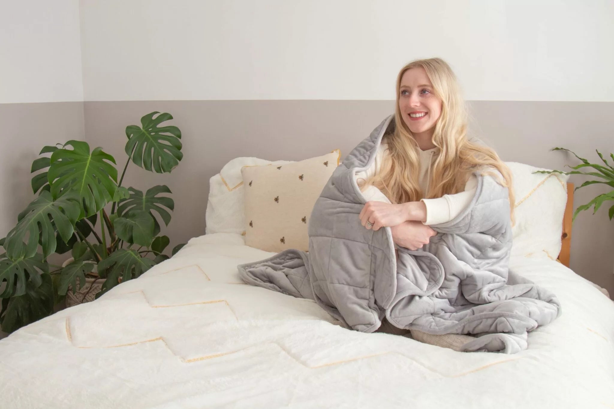 Woman using light grey weighted blanket while sitting on a bed